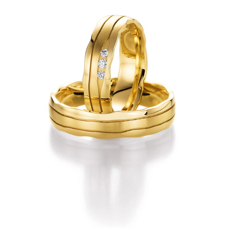 Elegante Trauringe aus Gelbgold mit sanft geschwungener Form und feinen Linien. Der Damenring ist mit drei Brillanten verziert und verleiht dem Ringset eine edle, harmonische Ausstrahlung.