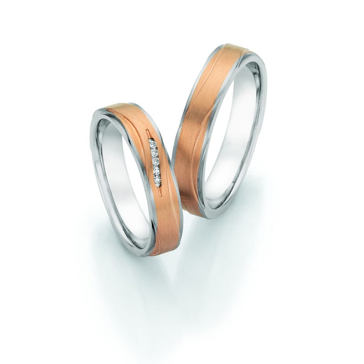 Elegante Trauringe aus Weiß- und Roségold mit geschwungenem Design. Der Damenring ist mit drei Brillanten besetzt und verleiht dem Ringset eine moderne und stilvolle Ausstrahlung.