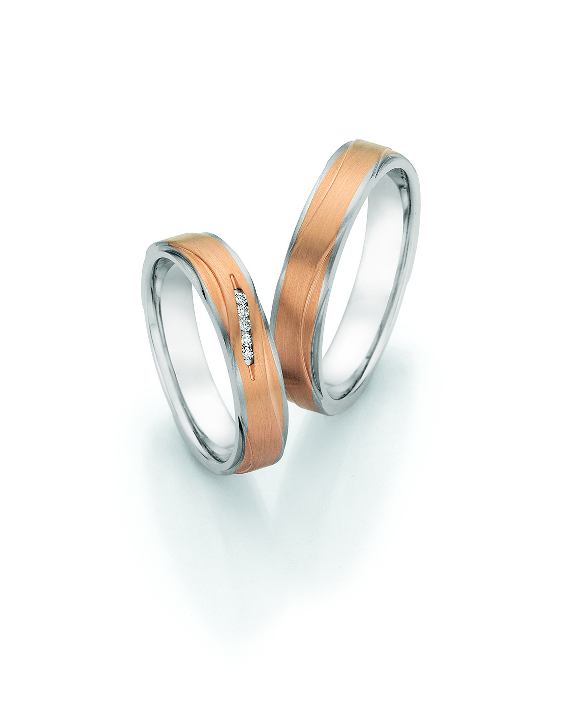 Elegante Trauringe aus Weiß- und Roségold mit geschwungenem Design. Der Damenring ist mit drei Brillanten besetzt und verleiht dem Ringset eine moderne und stilvolle Ausstrahlung.