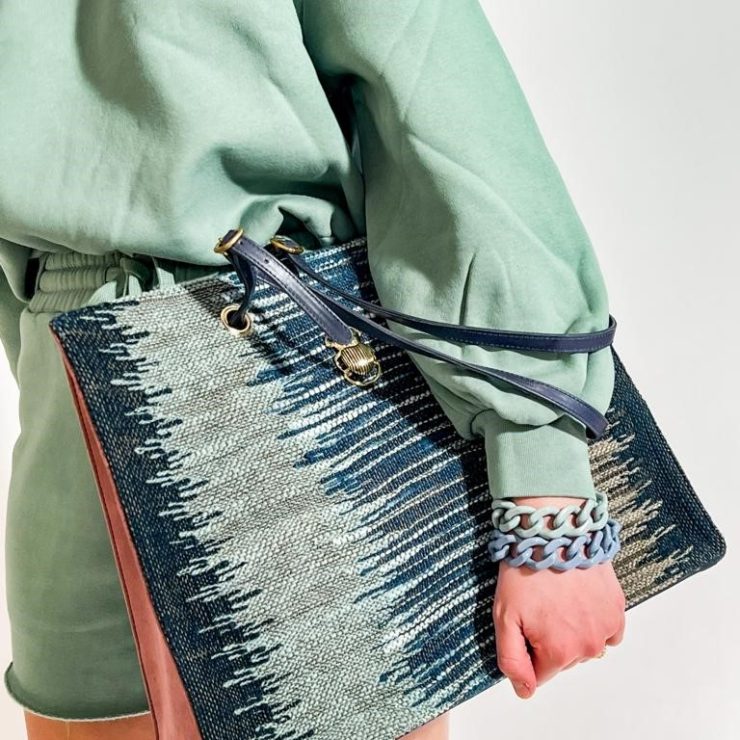 Person in mintgrünem Outfit trägt eine große gemusterte Handtasche in Blau- und Naturtönen. Farblich abgestimmte Armbänder in Blau und Mintgrün ergänzen den modernen und sommerlichen Look.