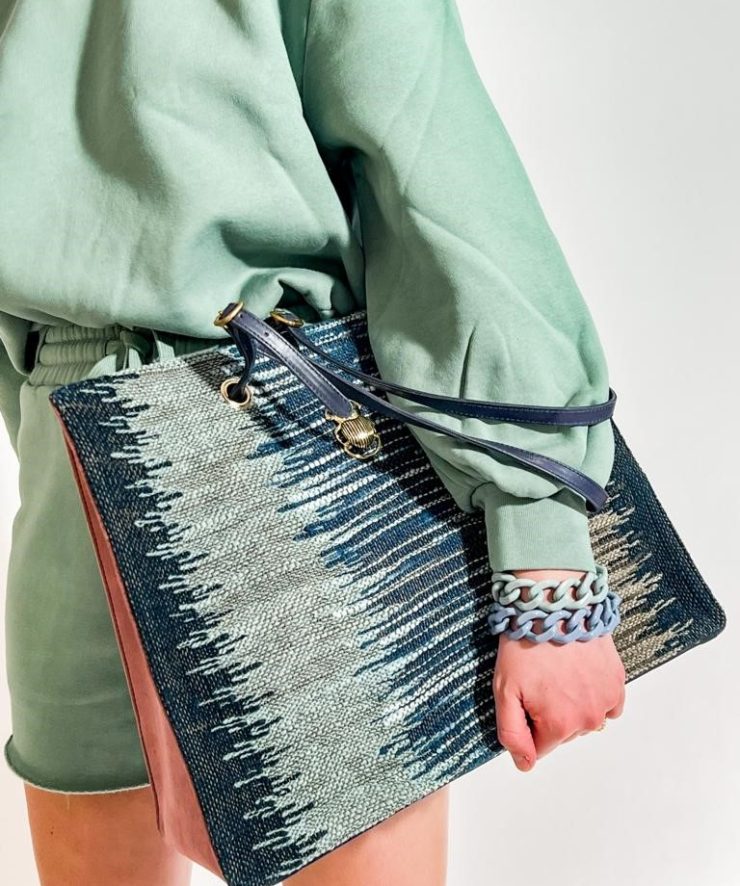 Person in mintgrünem Outfit trägt eine große gemusterte Handtasche in Blau- und Naturtönen. Farblich abgestimmte Armbänder in Blau und Mintgrün ergänzen den modernen und sommerlichen Look.