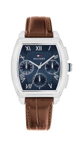 Tommy Hilfiger Armbanduhr mit silberfarbenem Tonneau-Gehäuse, blauem strukturiertem Zifferblatt, drei Multifunktions-Hilfszifferblättern für Wochentag, Datum und 24-Stunden-Anzeige, römischen Ziffern als Stundenmarkierungen und einem braunen Lederarmband auf hellem Hintergrund