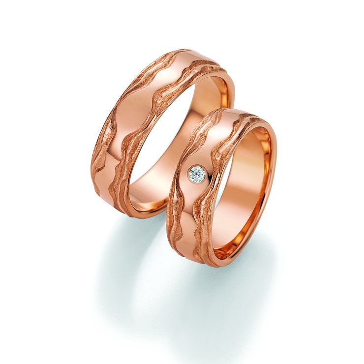 Außergewöhnliches Trauring-Set in warmer Roségoldoptik mit kunstvoller, wellenförmiger Oberflächenstruktur. Die organischen Linien verleihen den Ringen einen natürlichen und individuellen Charakter. Der Damenring wird durch einen funkelnden Brillanten stilvoll akzentuiert. Ein besonderes Symbol für Liebe, Verbundenheit und die gemeinsame Lebensreise.