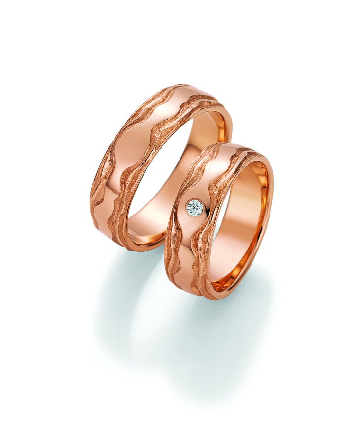 Außergewöhnliches Trauring-Set in warmer Roségoldoptik mit kunstvoller, wellenförmiger Oberflächenstruktur. Die organischen Linien verleihen den Ringen einen natürlichen und individuellen Charakter. Der Damenring wird durch einen funkelnden Brillanten stilvoll akzentuiert. Ein besonderes Symbol für Liebe, Verbundenheit und die gemeinsame Lebensreise.