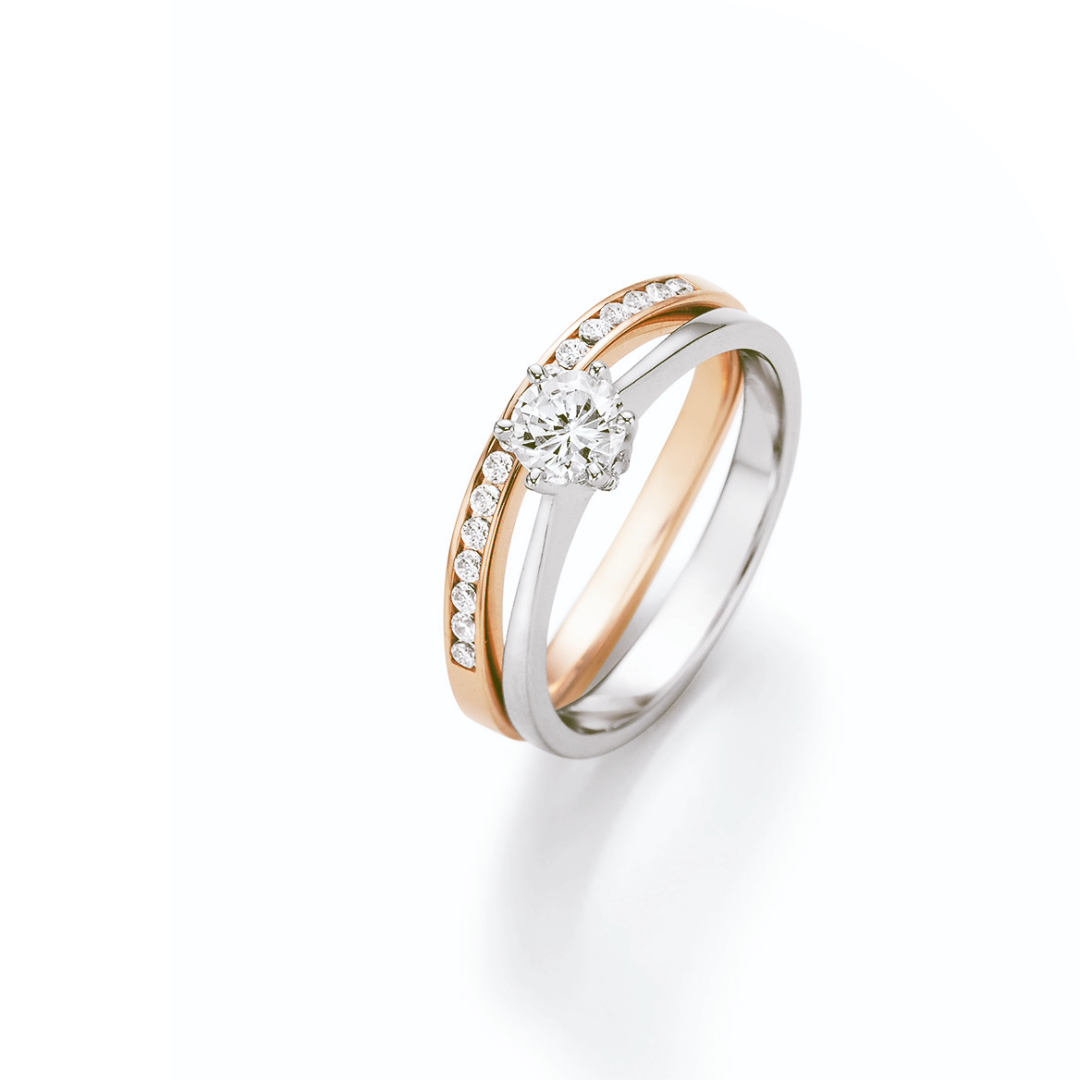 Eleganter Verlobungsring in Weiß- und Roségold mit funkelndem Brillantsolitär. Die geschwungene Ringschiene wird von einer Reihe fein gefasster Diamanten begleitet und verleiht dem Design eine harmonische Balance aus moderner Raffinesse und zeitloser Eleganz.