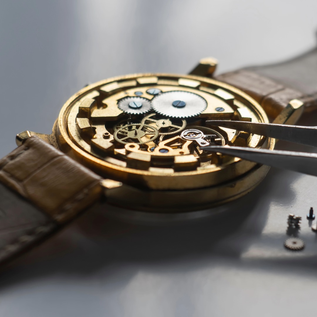 Geöffnete Armbanduhr mit sichtbarem mechanischem Uhrwerk, an dem mit einer Pinzette präzise Reparatur- oder Wartungsarbeiten durchgeführt werden