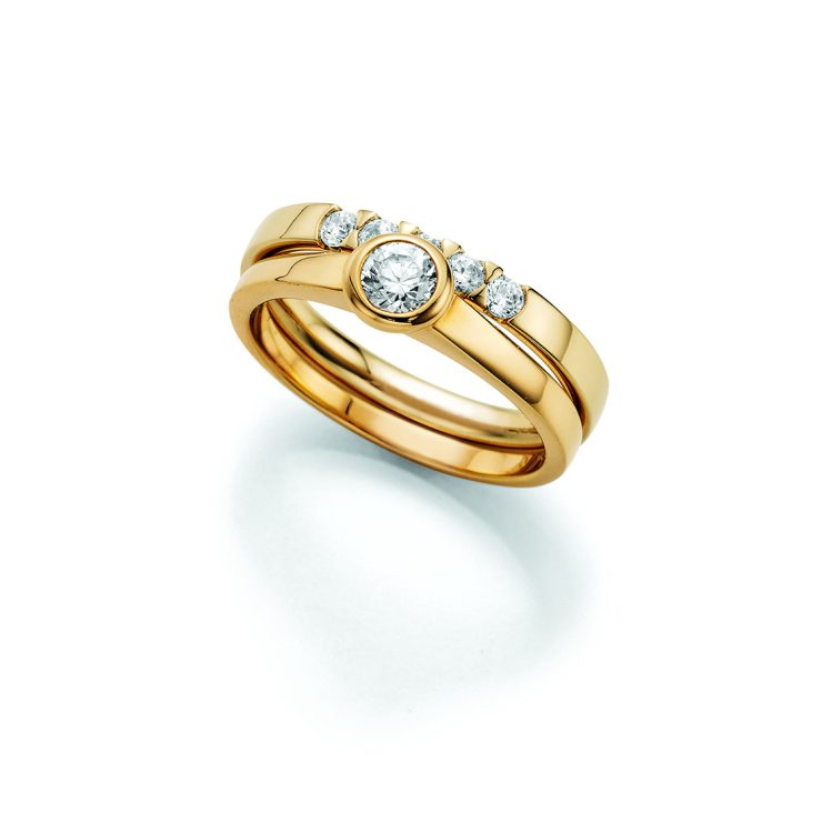Eleganter Ring aus Gelbgold mit zentralem Brillanten in Zargenfassung, flankiert von weiteren Diamanten auf der oberen Ringschiene. Das zweiteilige Design verleiht dem Schmuckstück eine moderne und luxuriöse Ausstrahlung.